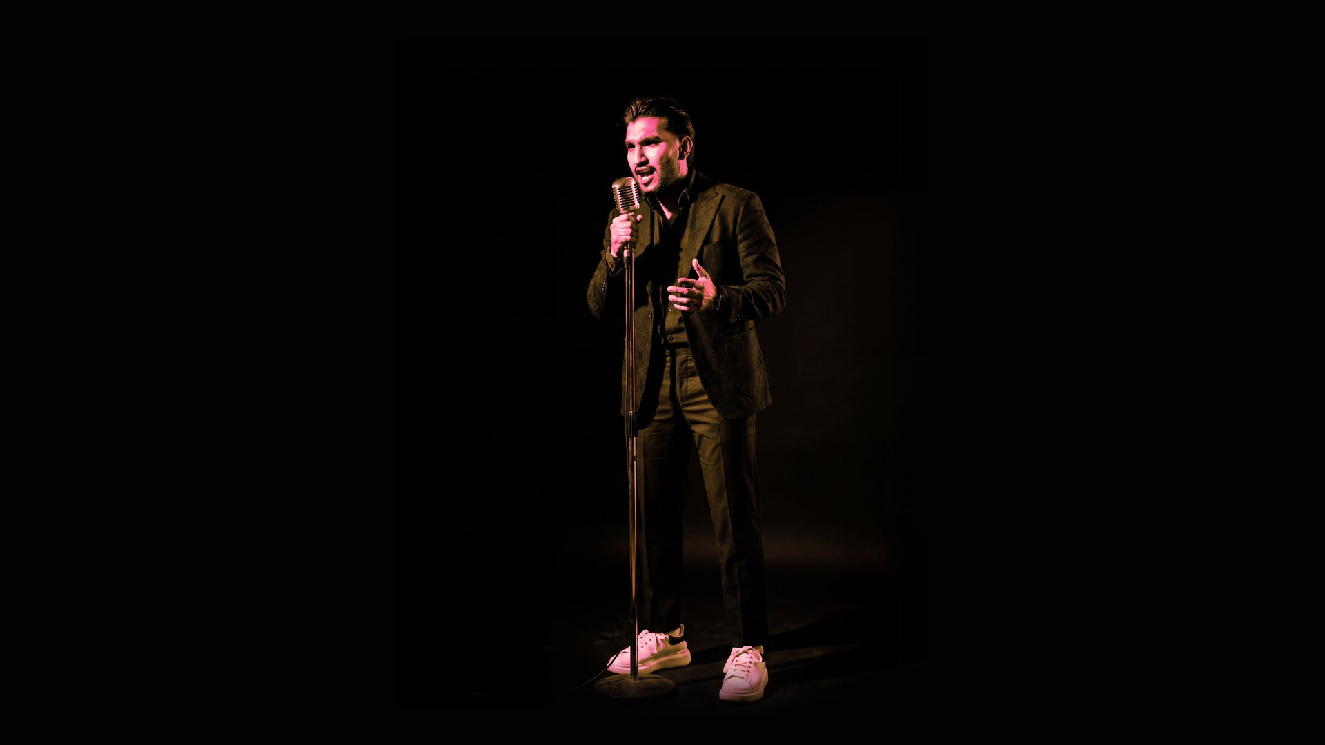 Sultan Bhatti at a vintage microphone under a spotlight, duotone