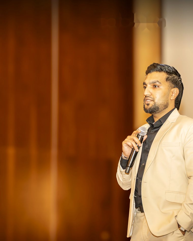 Sultan Bhatti speaking on stage with a microphone